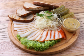 Нарезанное сало с солеными огурцами, горчичным соусом, ржаным хлебом, копченым сыром и зеленым салатом.